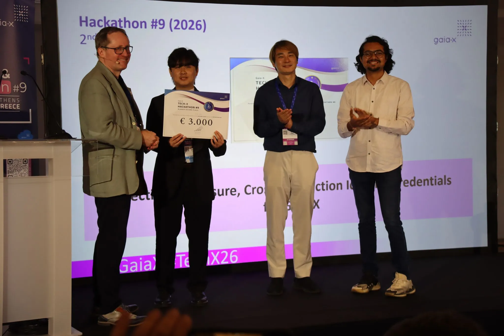 On stage at Gaia-X Tech-X & Hackathon #9 in Athens, holding the €3,000 second-place cheque with teammates, in front of the project title on screen.